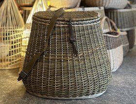 Ein grünlich eingefärbter, runder Wanderrucksack mit Deckel aus Weide mit zwei braunen, flachen Lederriemen.