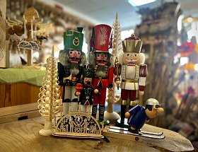 Etwa dreissig Zentimeter hohe erzgebirgische Nussknacker in schwarzer, roter und goldener Farbe sind in der Bildmitte zu sehen. Davon steht ein Miniatur-Schwibbogen mit zwei Bergmännern, Schnitzer und Klöppelfrau. Eingerahmt ist das Ensemble von zwei Räuchermännern und zwei Spanbäumen.