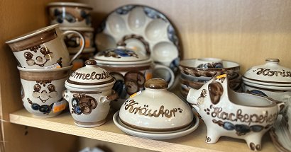 Unterschiedliche erzgebirgische, handgetöpferte Heyde-Keramik steht ebenfalls in einem Schrank. Motive wie Tassen, Suppenterrinen, Butterdose, Honigbehälter und Eiertellern zeigen eine große Auswahl dieser formschönen und bemalten Keramik.
