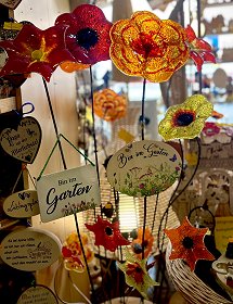 Rote und gelbe Glasblumen für Garten und Blumentöpfe zeigen sich auf diesem farbenfrohen Bild. Die handgefertigten, leuchtenden Objekte verraten auf kleinen Schildchen beispielsweise, dass man im Garten ist.