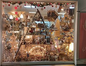 Das linke Schaufenster unseres Geschäftes mit beleuchtetem Schwibbbogen und weihnachtlicher Girlande sowie anderen erzgebirgischen Holzkunstartikeln in weihnachtlicher Beleuchtung